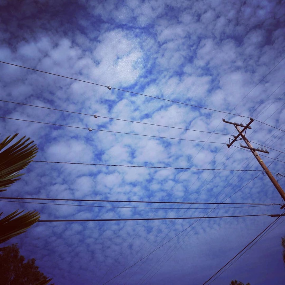 Utility wires crossing a vivid blue cloud-filled sky