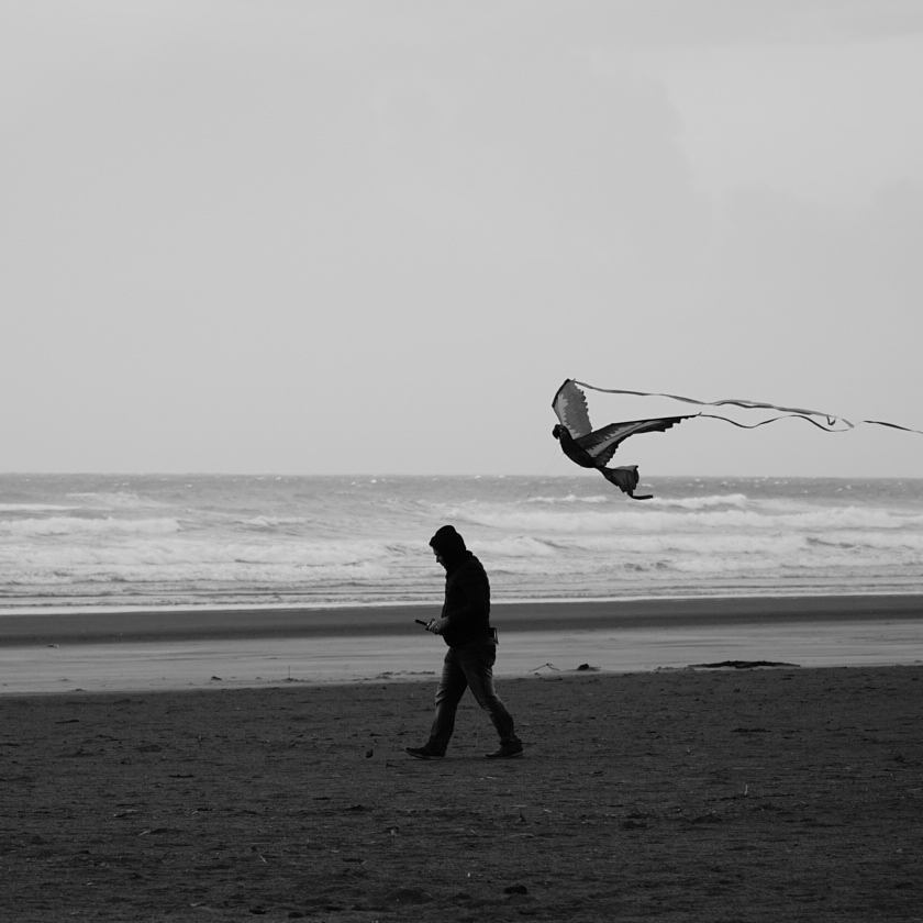 A person walking along the beach beneath a flying kite